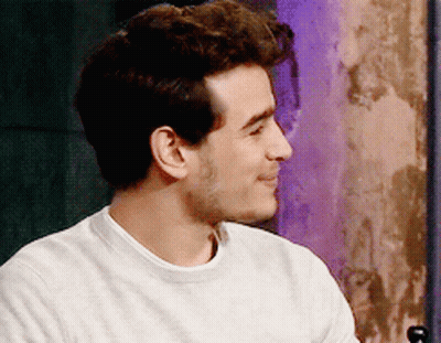A Man Wearing A White Sweater Is Smiling And Looking To The Side GIF