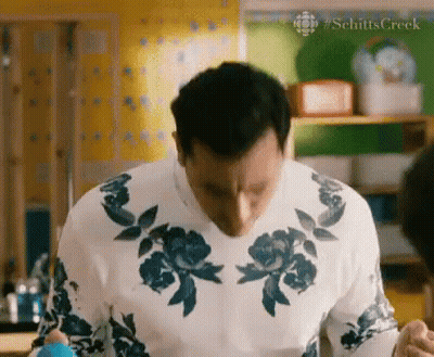 A Man Wearing A White Sweater With Blue Flowers On It Is Standing In A Kitchen GIF