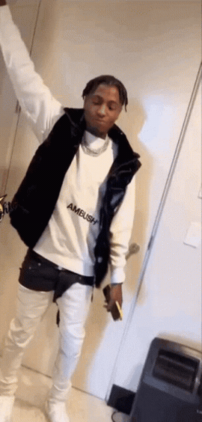 A Man Wearing A White Sweatshirt And A Black Vest Is Standing In A Room With His Arms In The Air . GIF