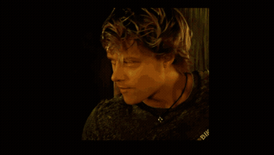 A Man Wearing A White T-Shirt Is Sitting In Front Of A Window Holding A Pair Of Gloves . GIF