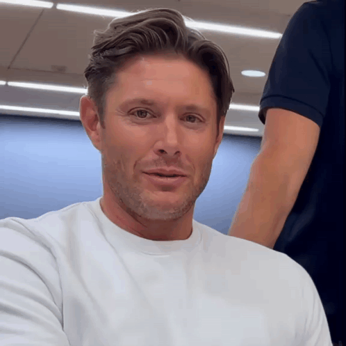 A Man Wearing A White T-Shirt Is Smiling For The Camera GIF