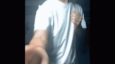 A Man Wearing A White T-Shirt Is Standing In The Dark GIF