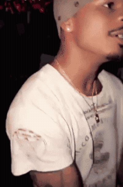 A Man Wearing A White T-Shirt With A Necklace Around His Neck And A Hat On GIF