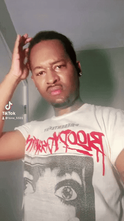 A Man Wearing A White T-Shirt With Graffiti On It Is Looking At The Camera GIF