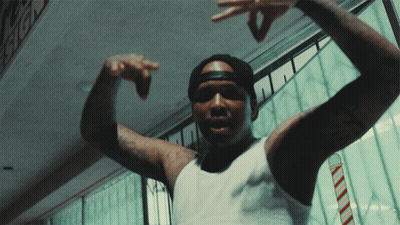 A Man Wearing A White Tank Top And A Black Hat Is Pointing His Fingers GIF