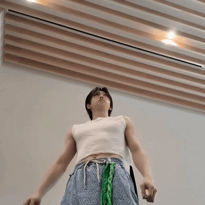 A Man Wearing A White Tank Top And Blue Shorts With A Green Bandana Around His Waist GIF