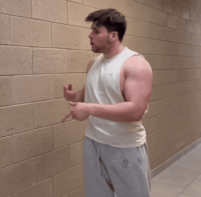 A Man Wearing A White Tank Top And Grey Shorts With The Letter S On The Bottom GIF