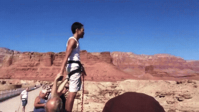A Man Wearing A White Tank Top And Shorts Is Standing In Front Of A Desert Landscape GIF