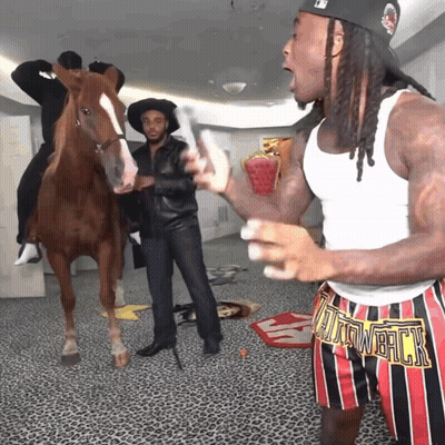 A Man Wearing A White Tank Top And Shorts That Say ' Tain Whack ' Stands In Front Of A Horse GIF