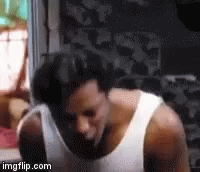 A Man Wearing A White Tank Top Is Standing In A Room . GIF