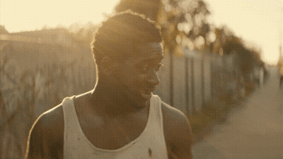 A Man Wearing A White Tank Top Is Walking Down A Road GIF