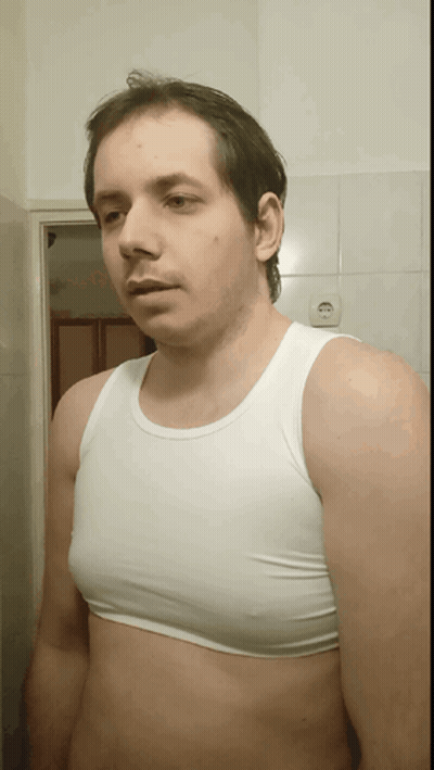 A Man Wearing A White Tank Top Stands In Front Of A White Tiled Wall GIF