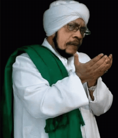 A Man Wearing A White Turban And A Green Scarf Is Praying With His Hands Together GIF
