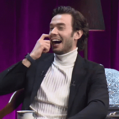 A Man Wearing A White Turtleneck And A Black Jacket Is Smiling GIF