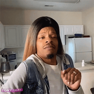 A Man Wearing A Wig And A Denim Vest Is In A Kitchen . GIF