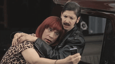 A Man Wearing A Wig And A Leather Jacket Is Standing Next To Another Man Wearing A Leather Jacket . GIF