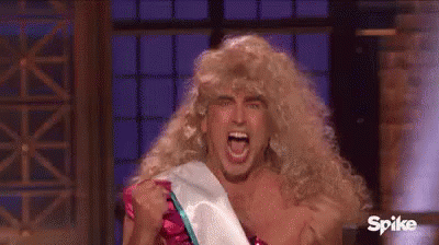 A Man Wearing A Wig And A Sash Is Screaming While Holding His Fist Up In The Air . GIF