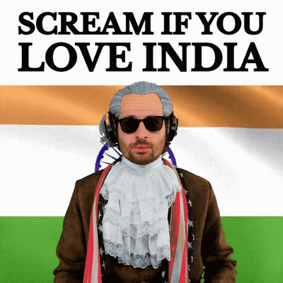A Man Wearing A Wig And Sunglasses Stands In Front Of A Flag And A Sign That Says Scream If You Love India GIF