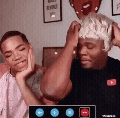 A Man Wearing A Wig Is Sitting Next To Another Man . GIF