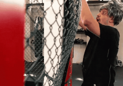 A Man Wearing A Wig Is Standing In Front Of A Chain Link Fence In A Gym GIF