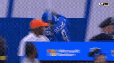 A Man Wearing A Williams Jersey Stands In Front Of A Fox Nfl Sign GIF
