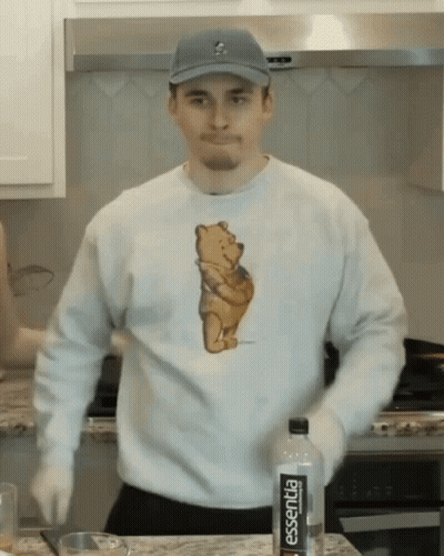 A Man Wearing A Winnie The Pooh Shirt Is Standing In Front Of A Bottle Of Essentia GIF