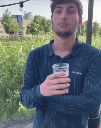 A Man Wearing A Woodbird Shirt Is Holding A Glass Of Beer . GIF