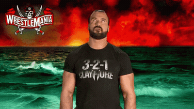 A Man Wearing A Wrestlemania T-Shirt Stands In Front Of A Stormy Ocean GIF