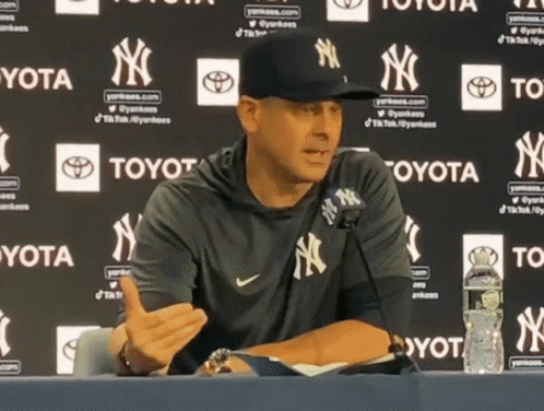 A Man Wearing A Yankees Hat Is Sitting At A Table GIF