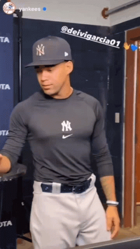 A Man Wearing A Yankees Shirt And Hat Stands In A Room GIF