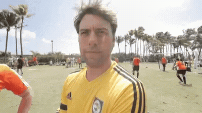A Man Wearing A Yellow Adidas Shirt Stands In Front Of A Soccer Field GIF