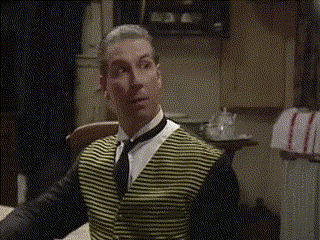 A Man Wearing A Yellow And Black Striped Vest And Tie Is Sitting At A Table GIF
