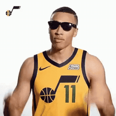 A Man Wearing A Yellow Basketball Jersey And Sunglasses Is Standing In Front Of A White Background . GIF