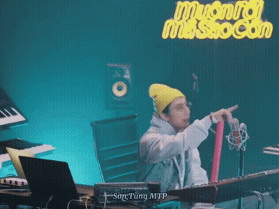 A Man Wearing A Yellow Beanie And Glasses Is Standing In Front Of A Microphone . GIF