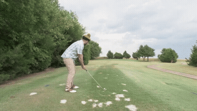 A Man Wearing A Yellow Beanie Is Swinging A Golf Club On A Golf Course GIF