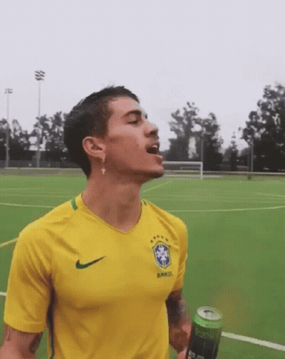 A Man Wearing A Yellow Brasil Shirt Is Drinking From A Green Can GIF