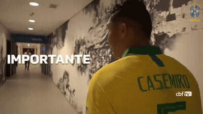 A Man Wearing A Yellow Casemiro Shirt Stands In A Hallway GIF