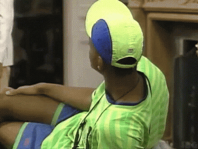 A Man Wearing A Yellow Hat And A Green Shirt Is Sitting On A Couch . GIF