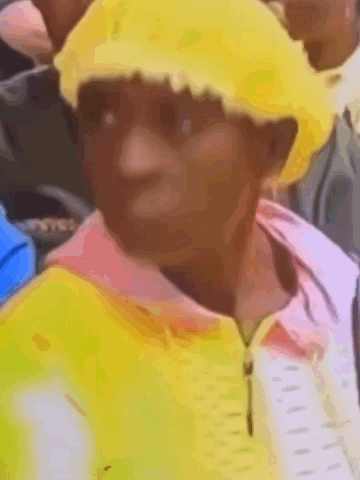 A Man Wearing A Yellow Hat And A Pink Shirt Is Standing In A Crowd . GIF