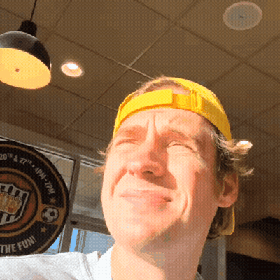 A Man Wearing A Yellow Hat Stands In Front Of A Sign That Says ' Fun ' On It GIF