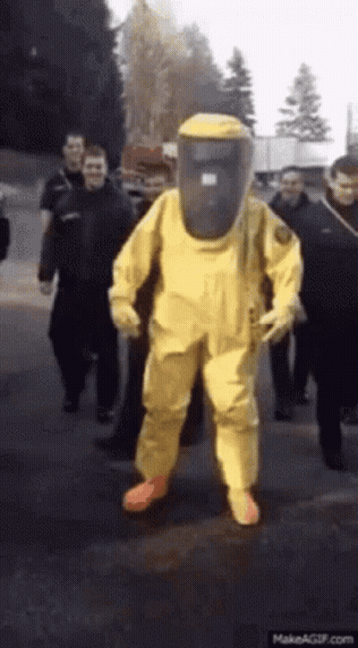 A Man Wearing A Yellow Hazmat Suit Is Walking Down The Street GIF