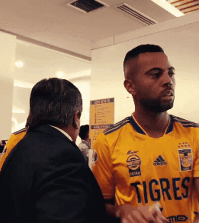 A Man Wearing A Yellow Jersey That Says Tigres Talks To Another Man GIF