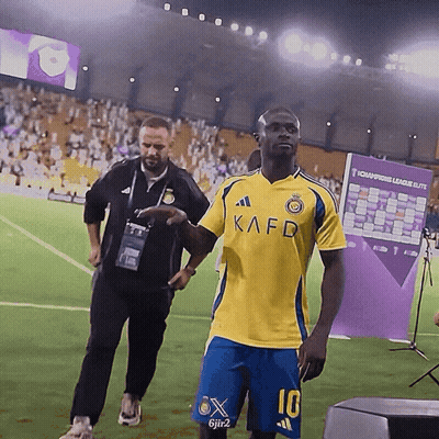 A Man Wearing A Yellow Kafd Shirt And Blue Shorts GIF