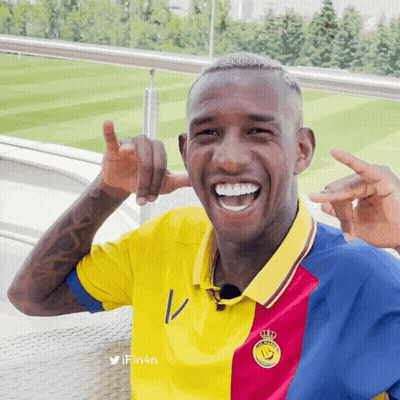 A Man Wearing A Yellow Red And Blue Shirt With A Crown On The Front GIF