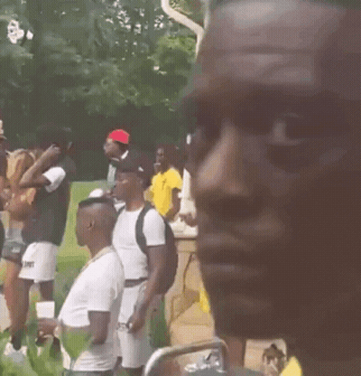 A Man Wearing A Yellow Shirt And A Gold Chain Is Standing In Front Of A Crowd Of People . GIF