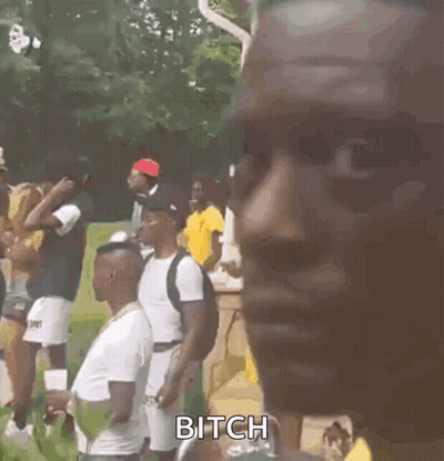 A Man Wearing A Yellow Shirt And A Necklace Is Standing In Front Of A Group Of People . GIF