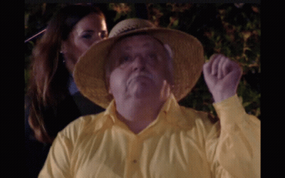 A Man Wearing A Yellow Shirt And A Straw Hat Is Being Kissed By A Woman GIF