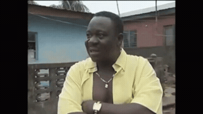 A Man Wearing A Yellow Shirt And A Watch Is Standing In Front Of A Building . GIF