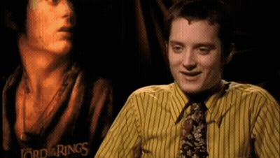 A Man Wearing A Yellow Striped Shirt And Tie Is Smiling In Front Of A Poster For The Lord Of The Rings GIF
