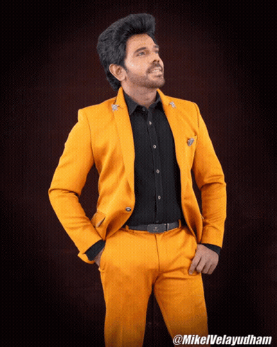A Man Wearing A Yellow Suit And A Black Shirt Is Standing With His Hands In His Pockets And The Hashtag Mikelvelayudham GIF